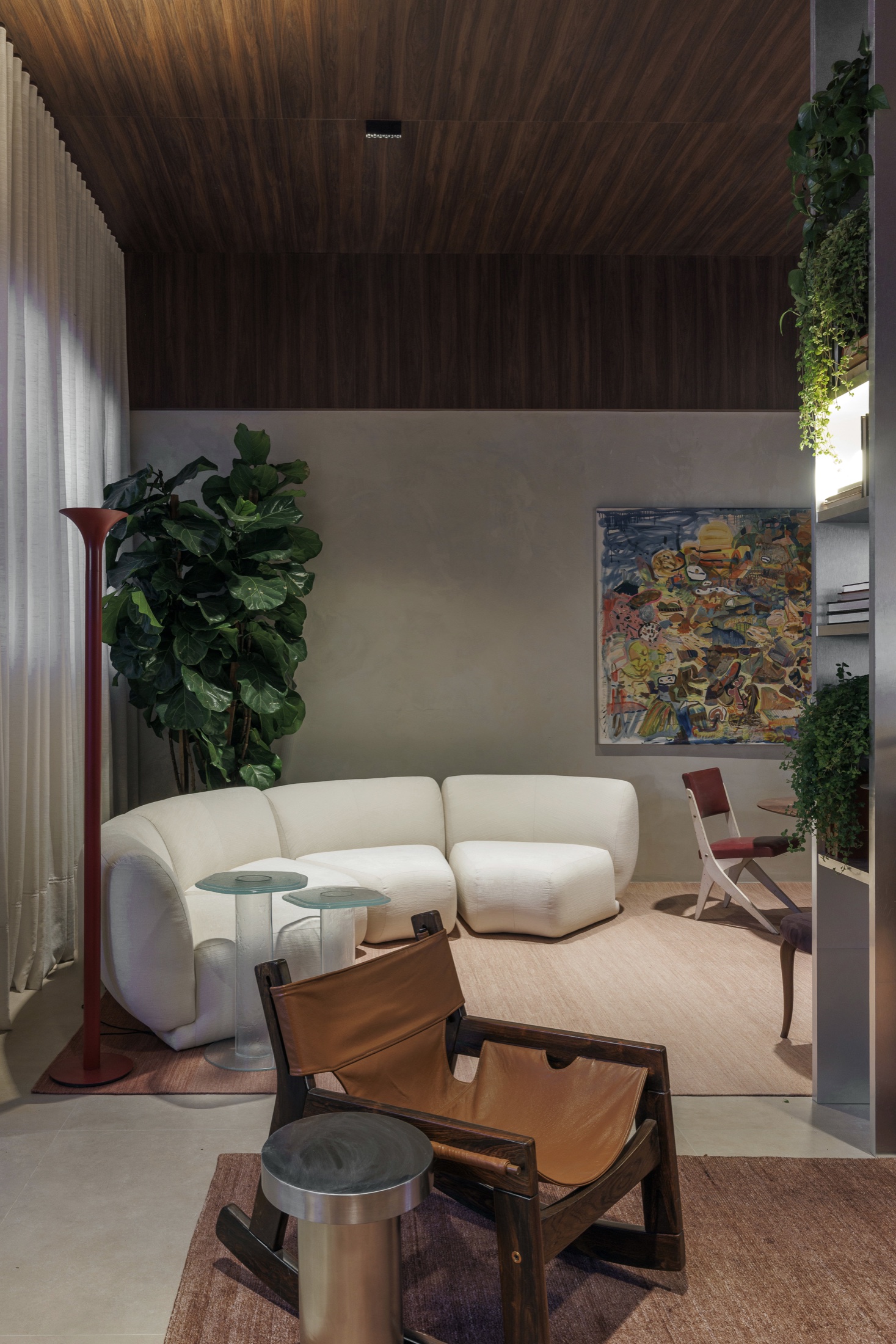 Sala com sofá angulado, luminária vermelha e mesa lateral em inox